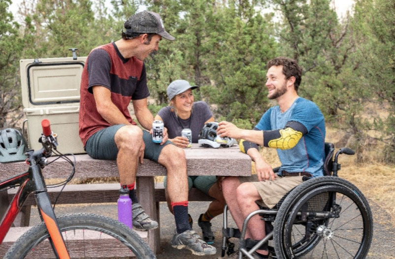 3 men sporty at park bench one in a wheel chair